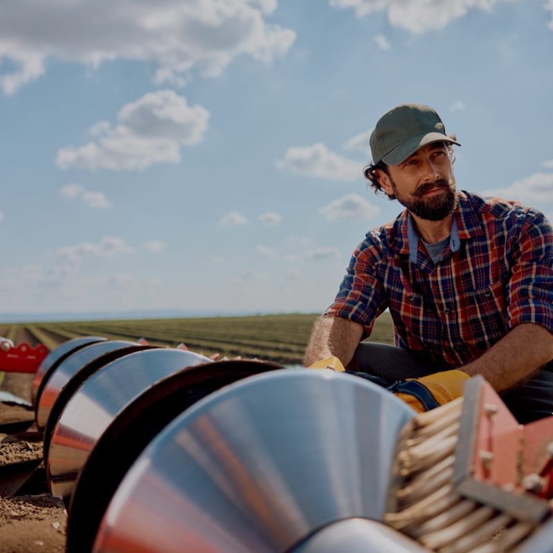Pensive agronomist setting up disc harrows on a tractor while plowing the land.